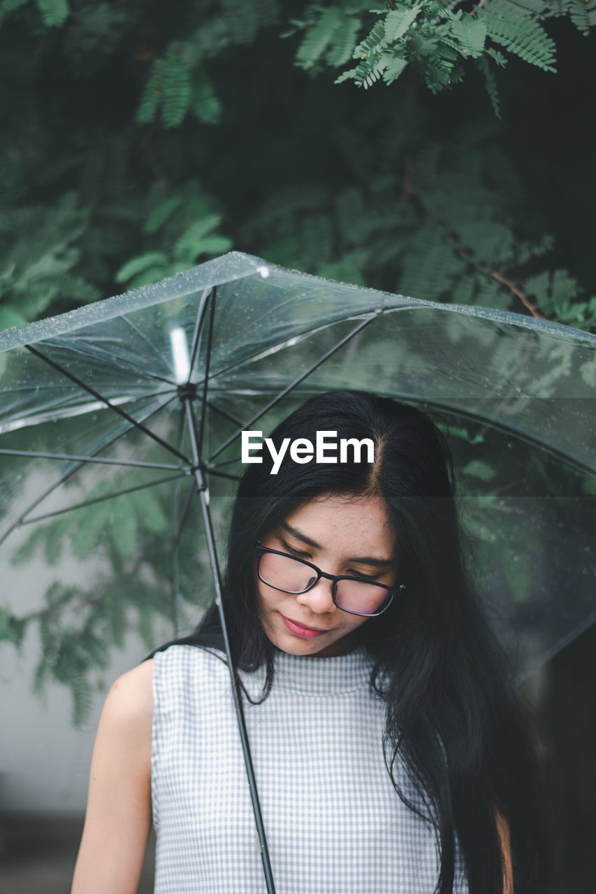 Young woman holding umbrella standing against trees