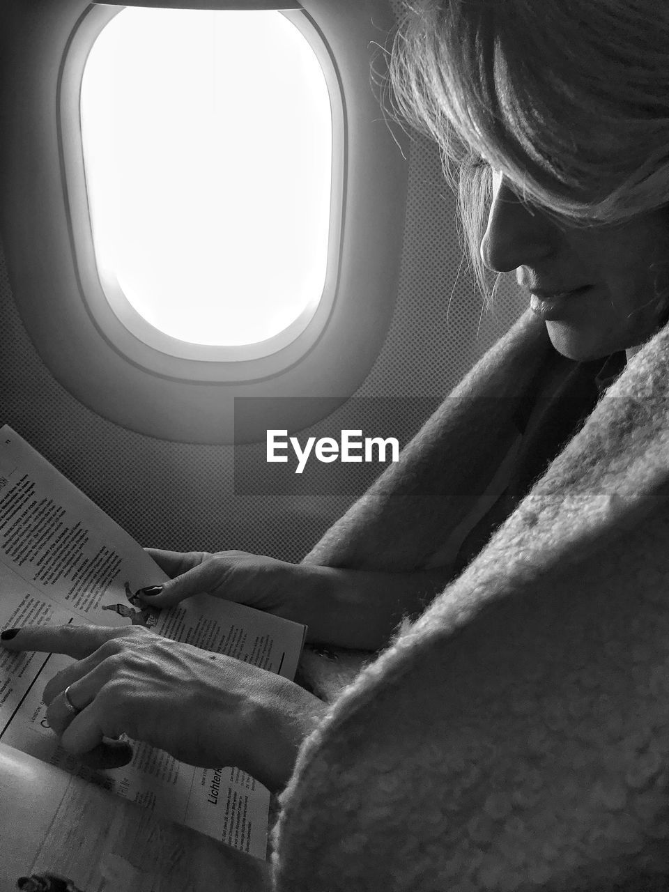 Side view of woman reading magazine in airplane