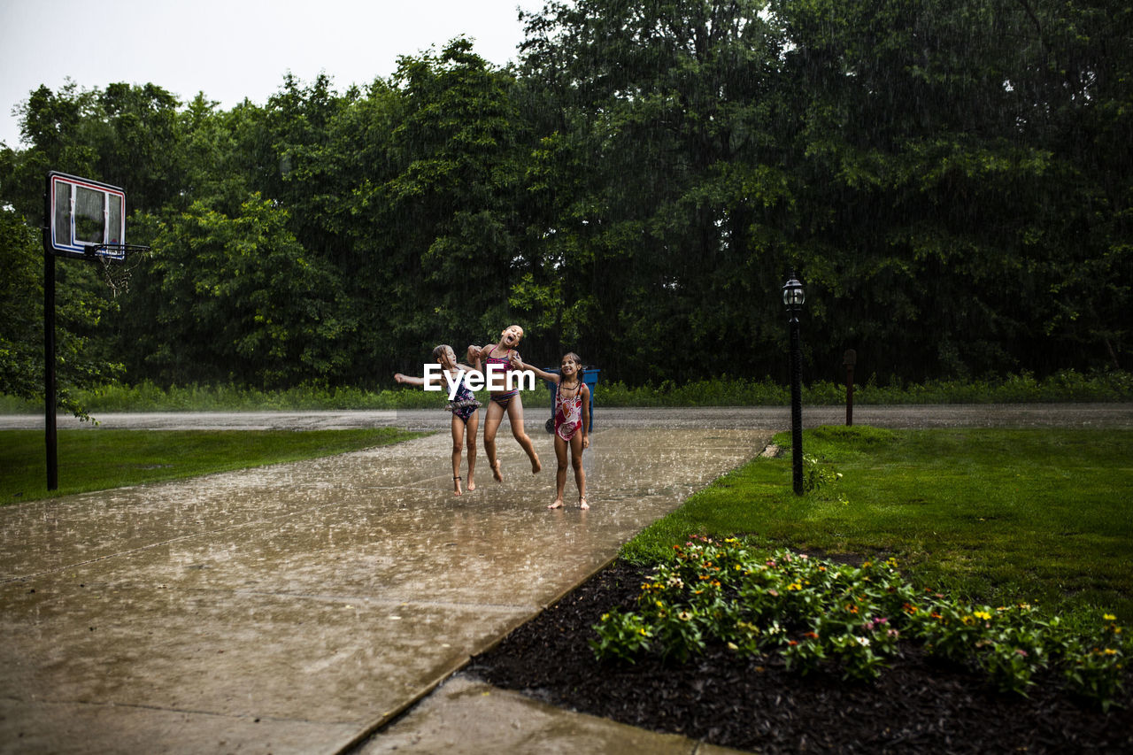 Full length of playful sisters dancing on footpath at park during rainfall