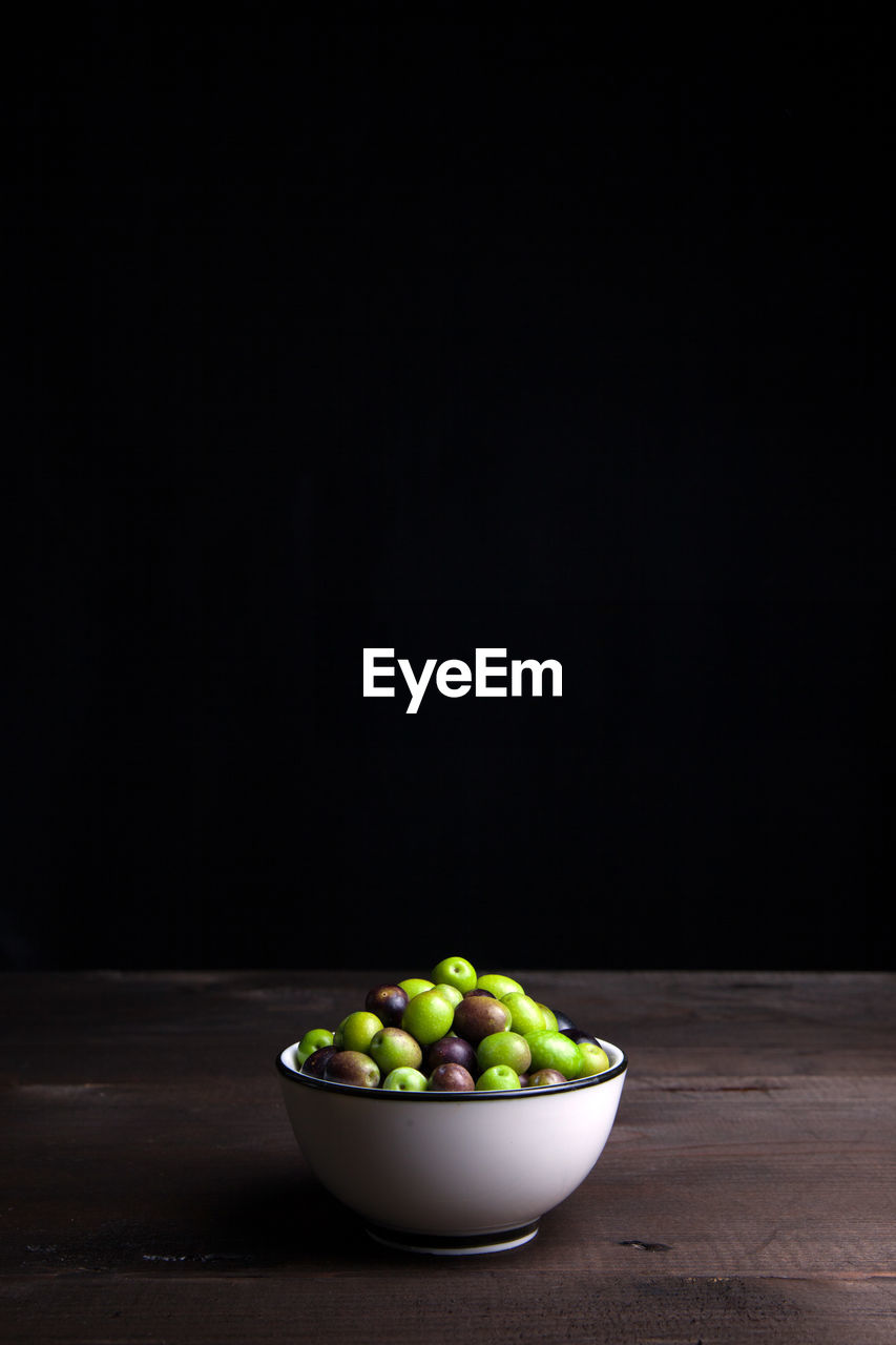 Close-up of green olives in bowl on table against black wall