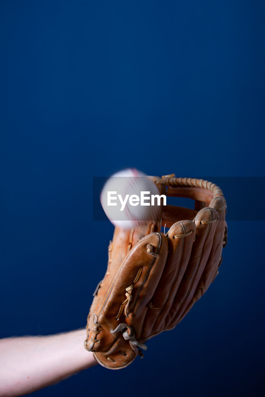 Close-up of hand holding bubble against blue background