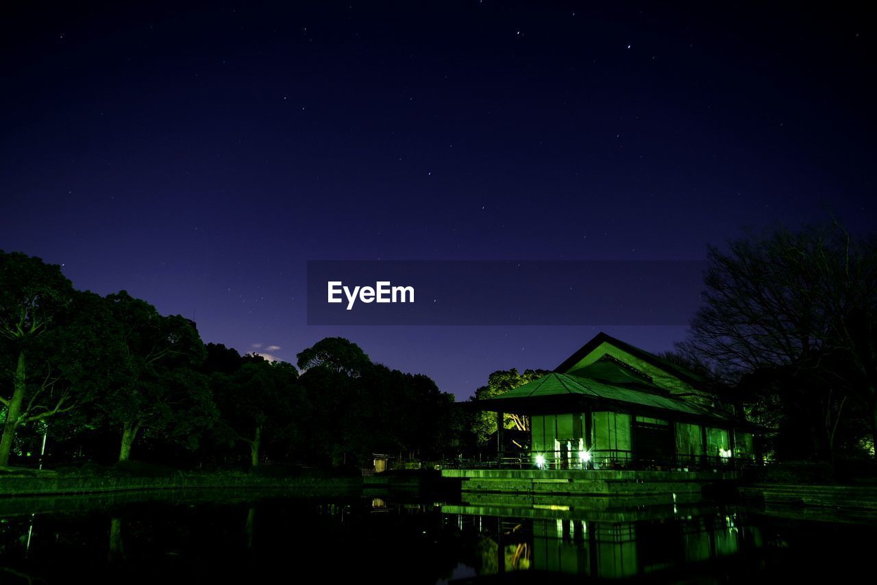 BUILT STRUCTURE BY TREES AGAINST SKY AT NIGHT