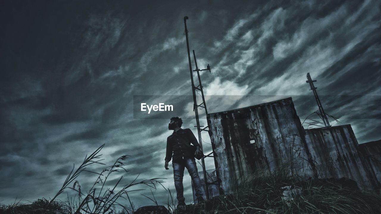 Low angle view of man standing against cloudy sky