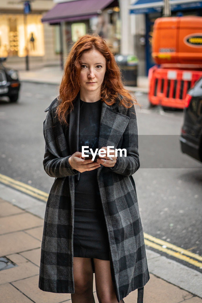 YOUNG WOMAN USING SMART PHONE WHILE STANDING ON STREET