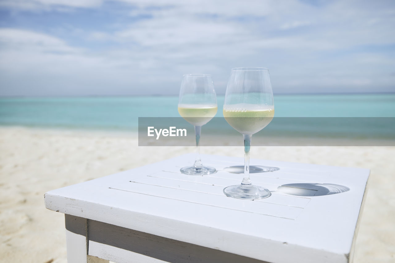 Two wineglass with white wine on wooden table against idyllic beach and turquoise sea.