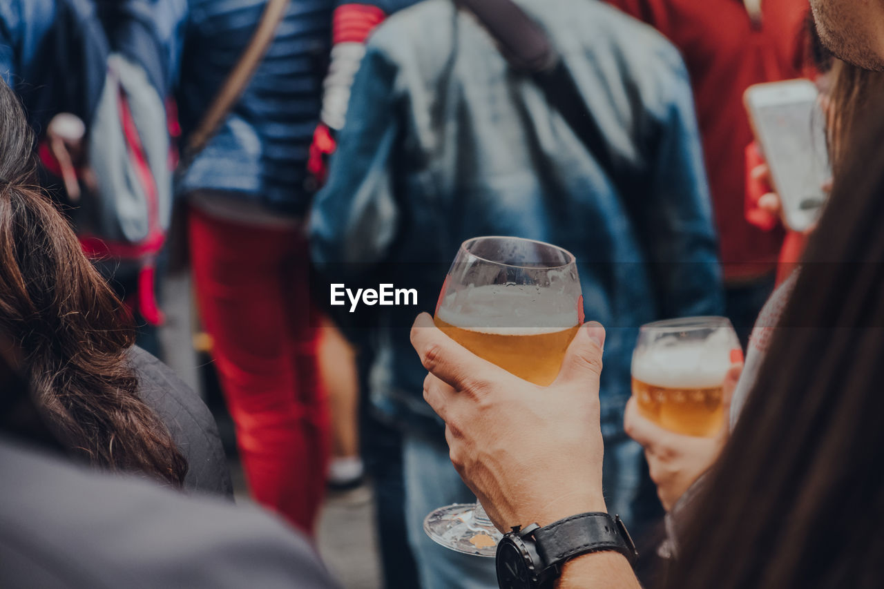 Hands holding glasses of beer on a street, selective focus on the foreground.