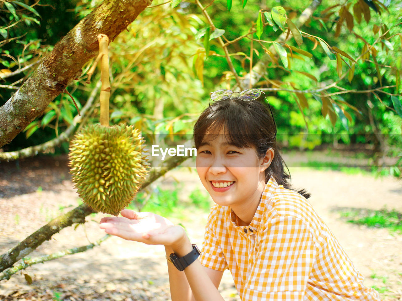 Portrait of smiling young woman showing fruit on tree