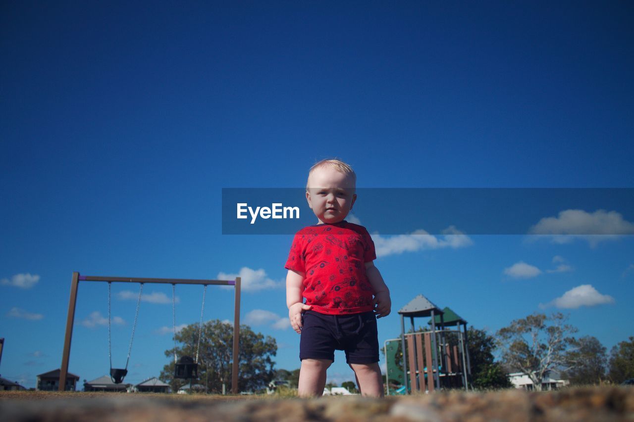 Portrait of boy standing on land against blue sky