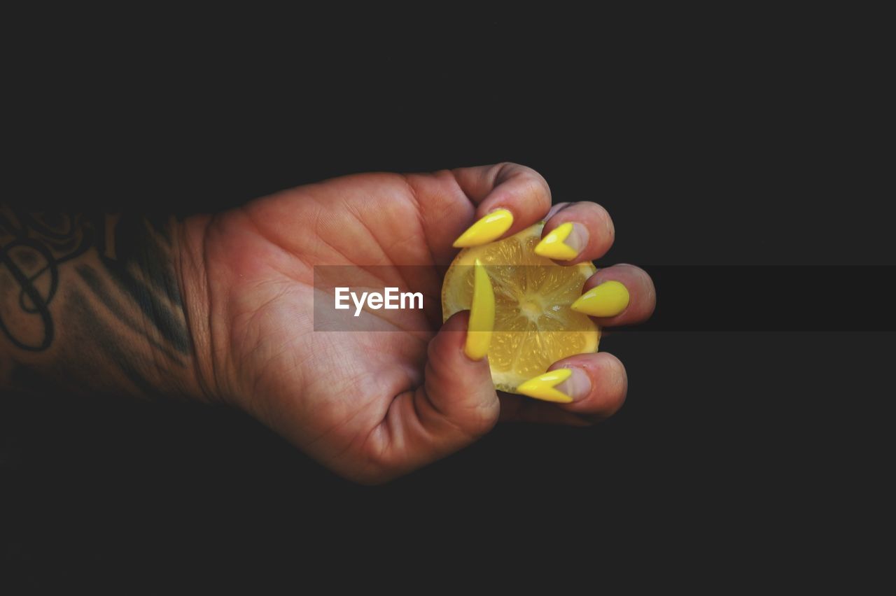 Close-up of hand holding lemon slice over black background