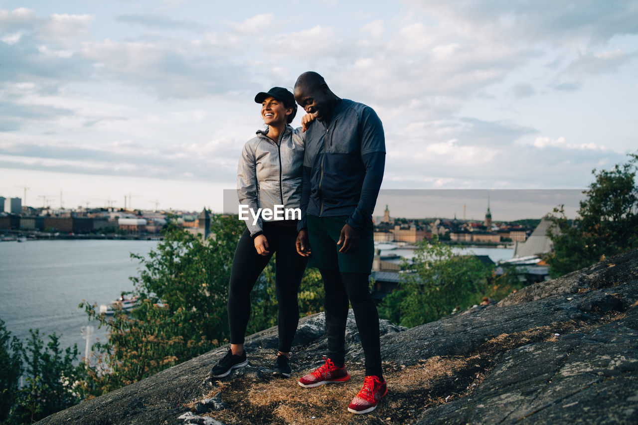 Full length of happy male and female athlete standing on hill against sky