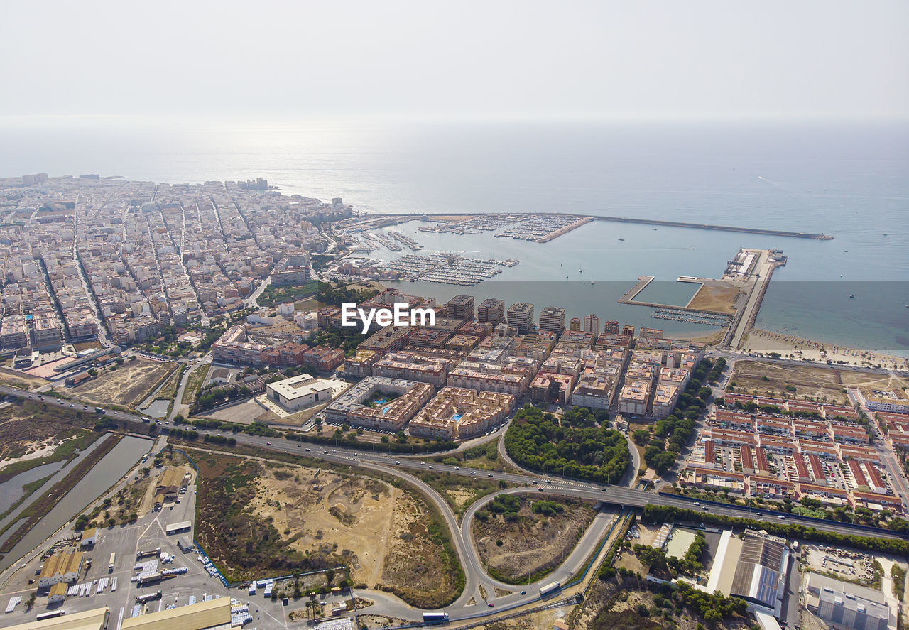 HIGH ANGLE VIEW OF CITYSCAPE AND SEA AGAINST SKY