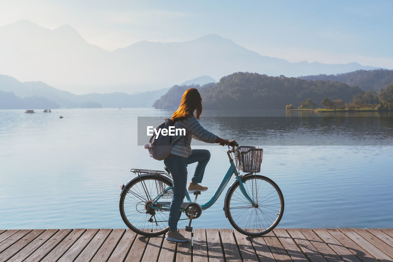Rear view of woman with bicycle by lake