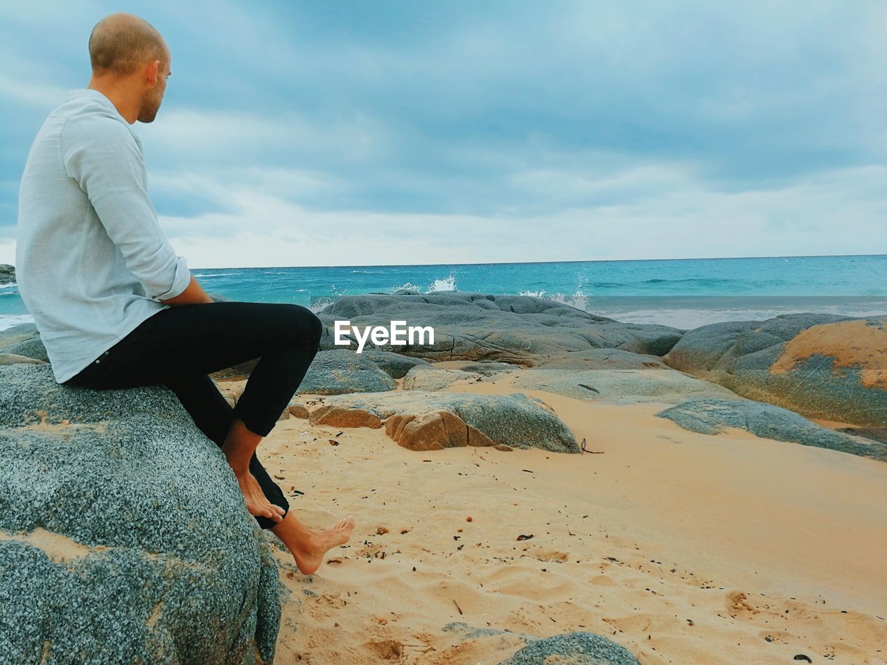 Man sitting on rock at beach against sky