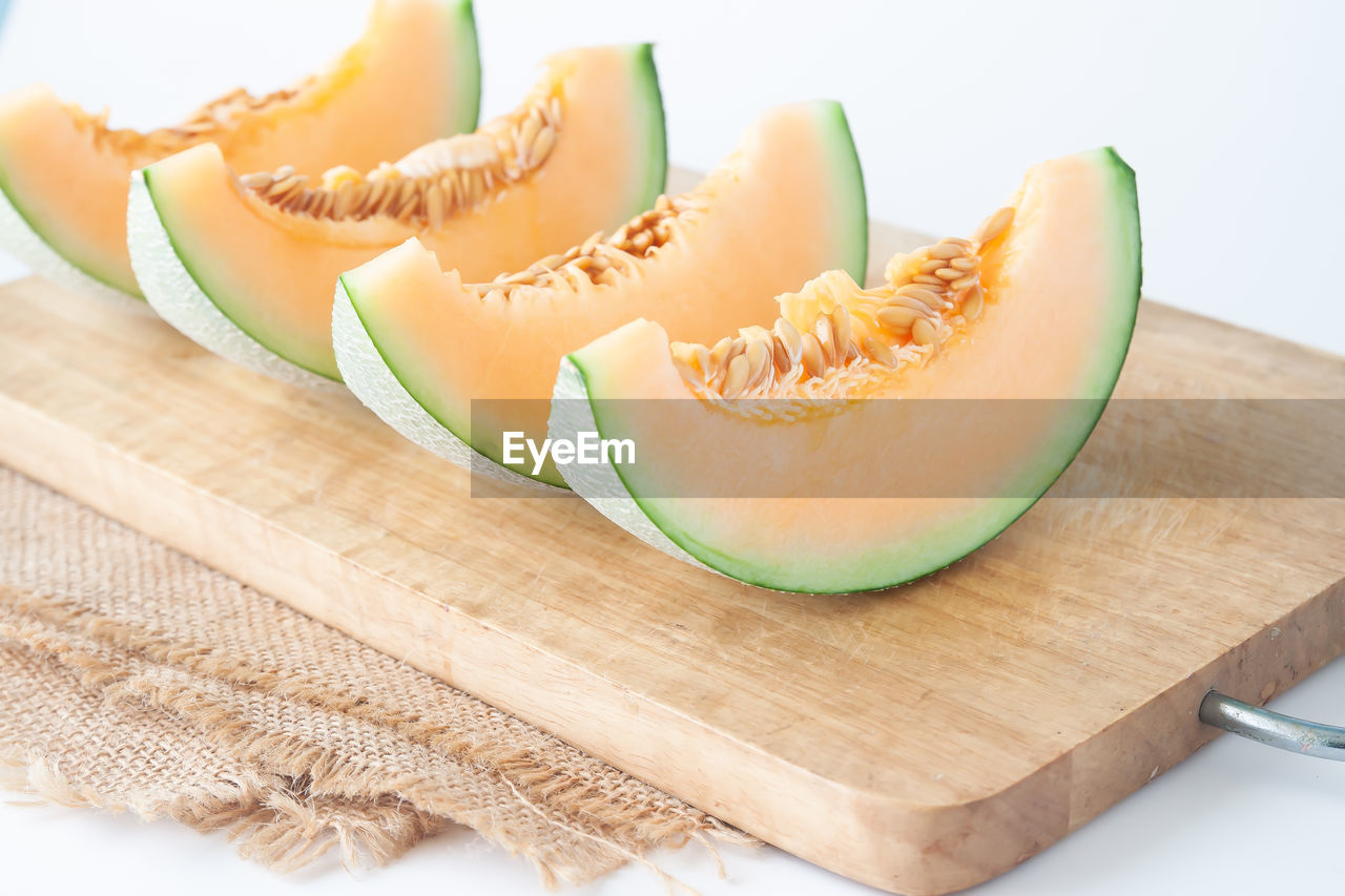 Close-up of cantaloupe slices on cutting board against white background