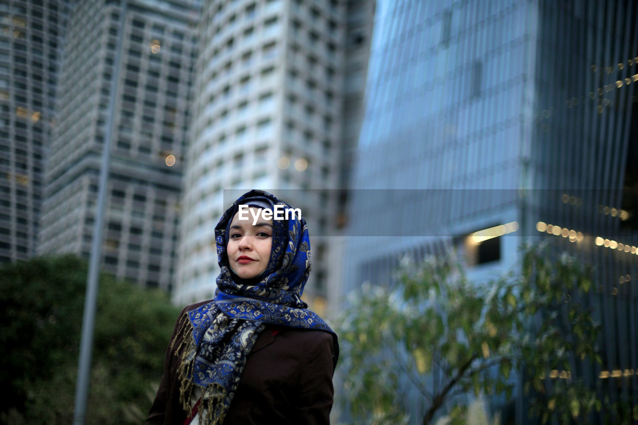 Low angle view of young woman looking away against buildings in city