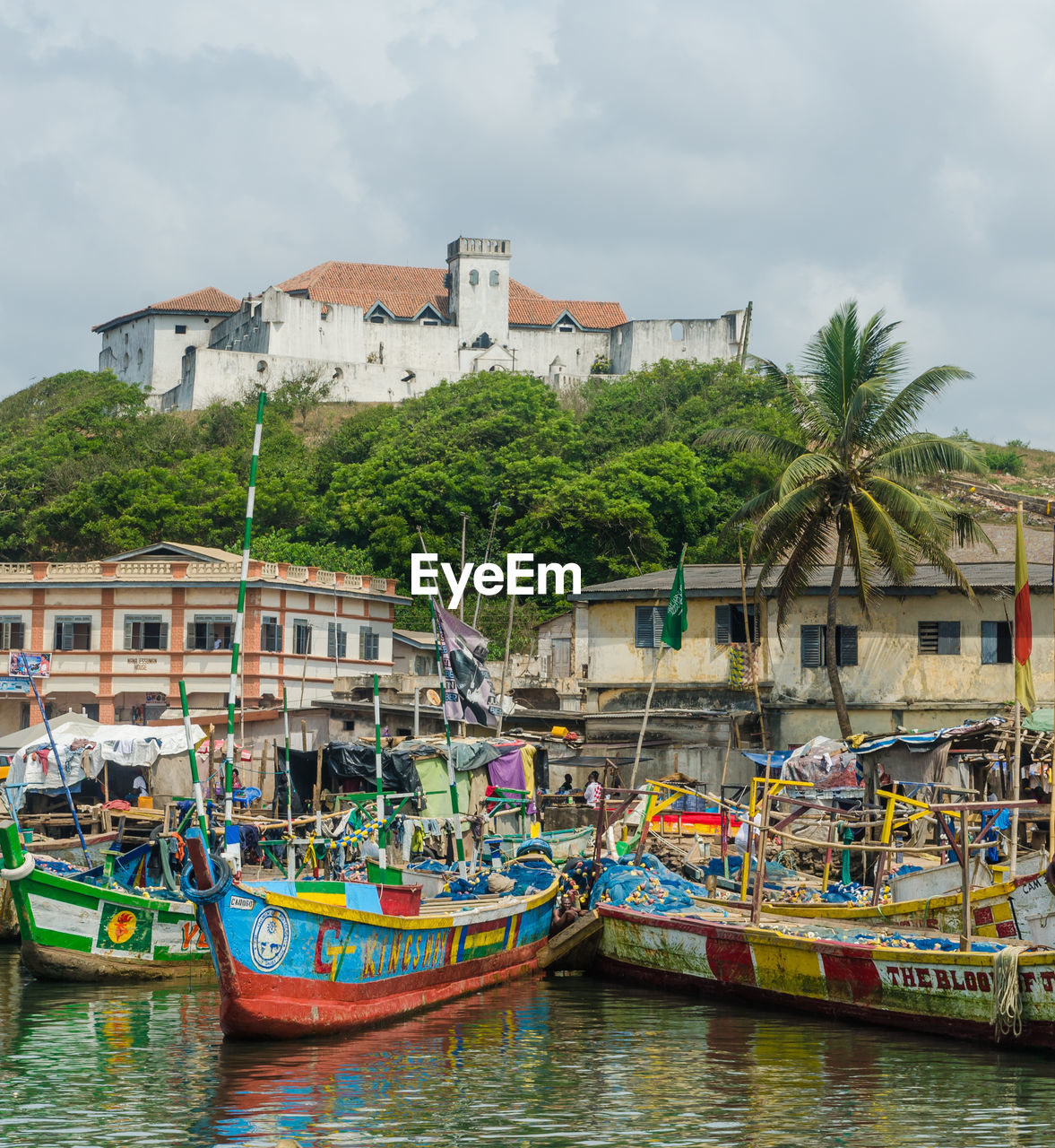 Boats moored in water against sky with fort coenraadsburg of elmina in background