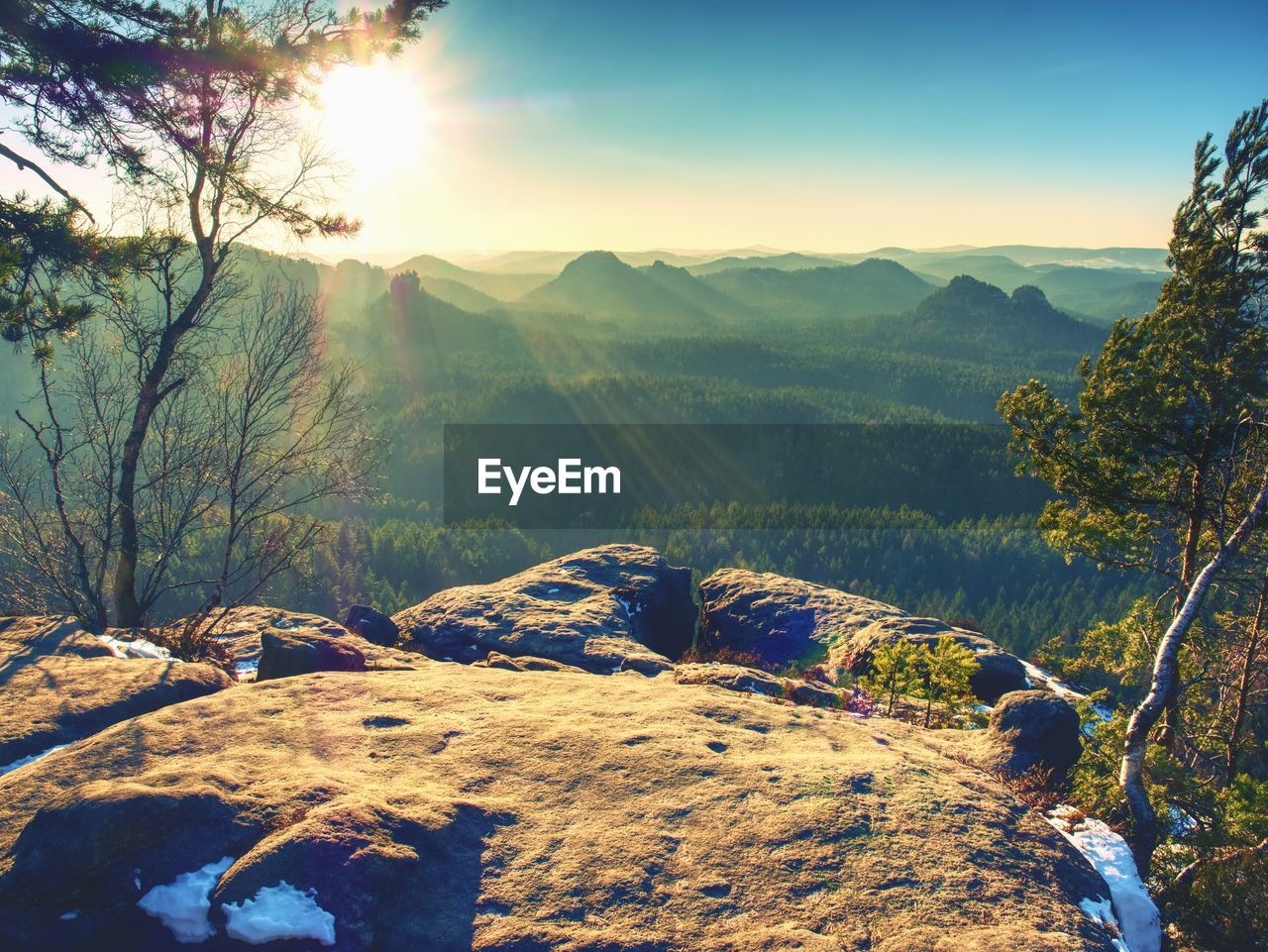 Spring morning nature. the cracked sandstone cliff above forest valley, daybreak sun at horizon.