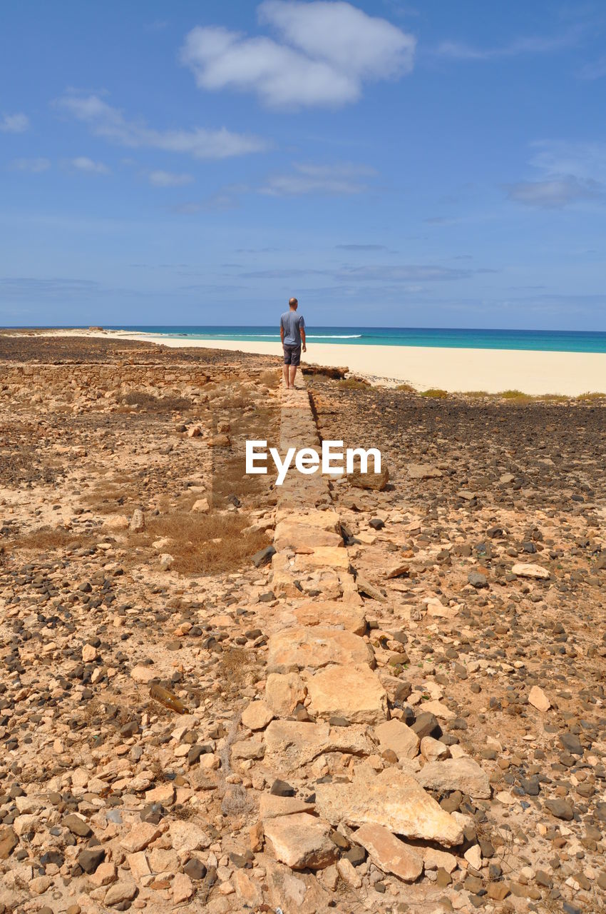 Rear view of man standing on pathway against sky at beach