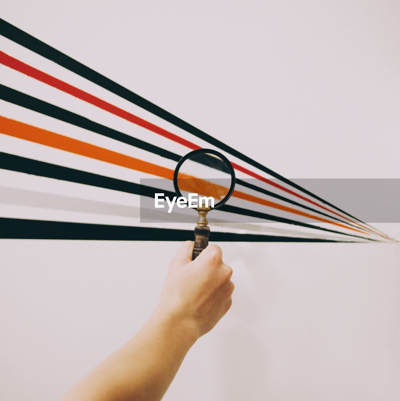 Cropped image of hand holding magnifying glass over pattern against white background