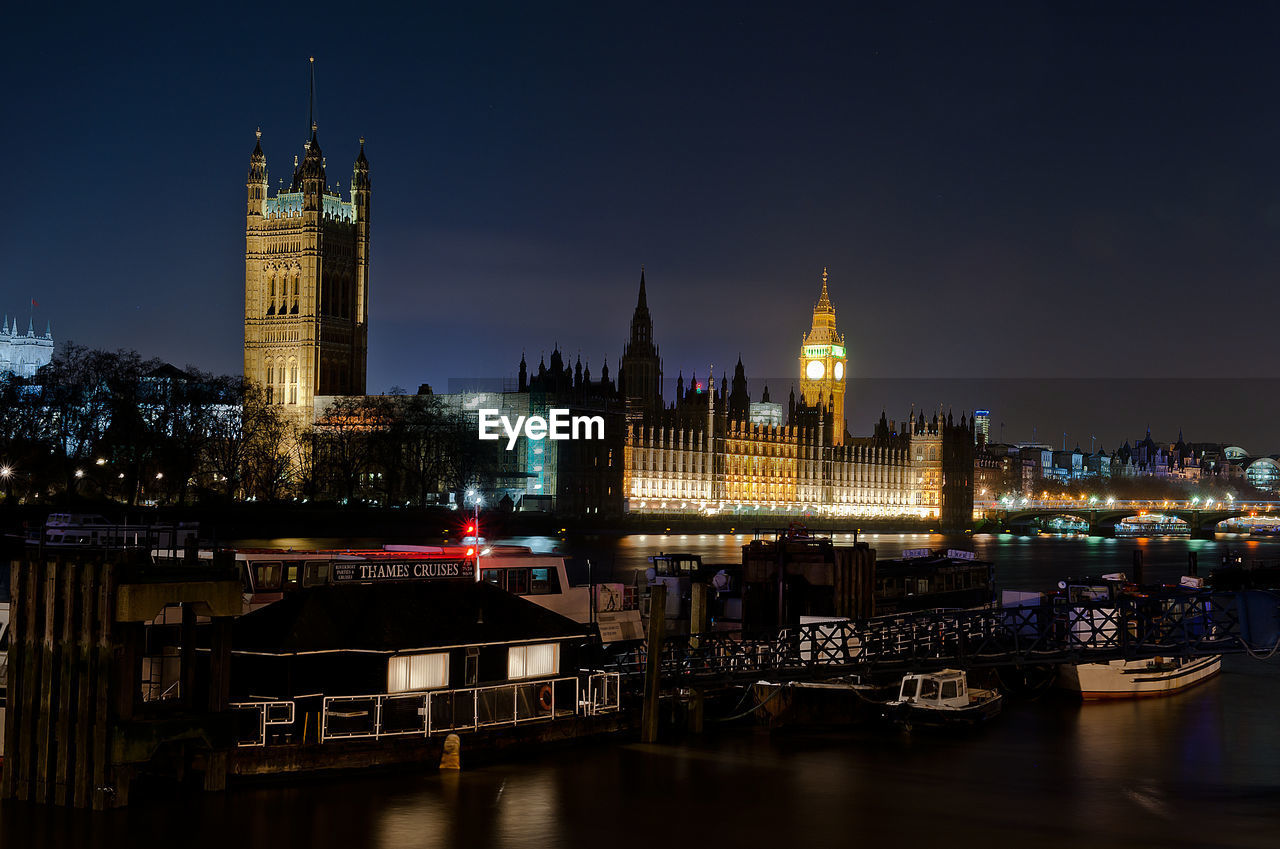 ILLUMINATED BUILDINGS BY RIVER IN CITY AGAINST SKY