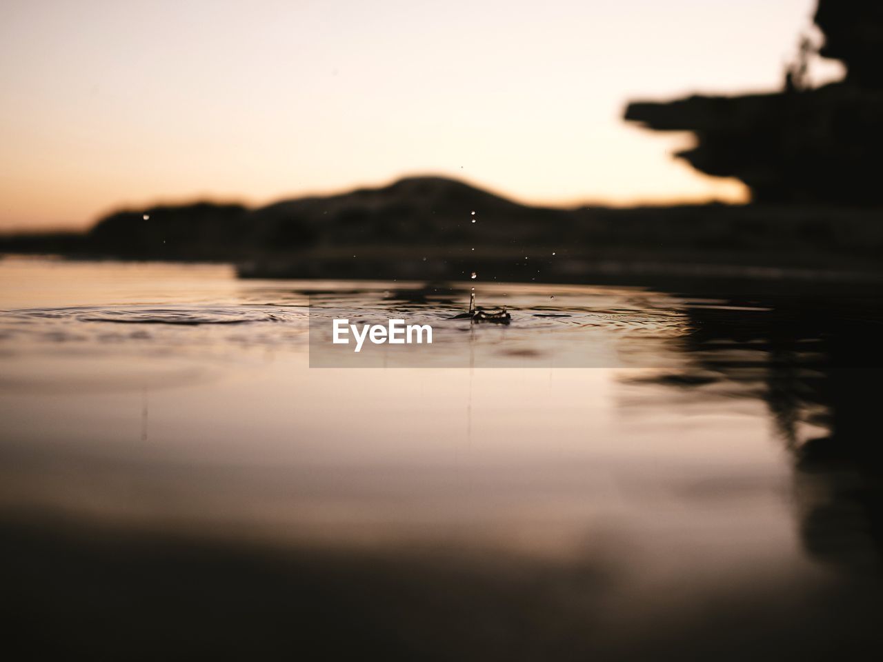 Close-up of drop falling on water at lake against sky during sunset
