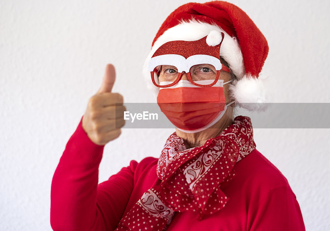 Portrait of woman wearing mask and santa hat against white background