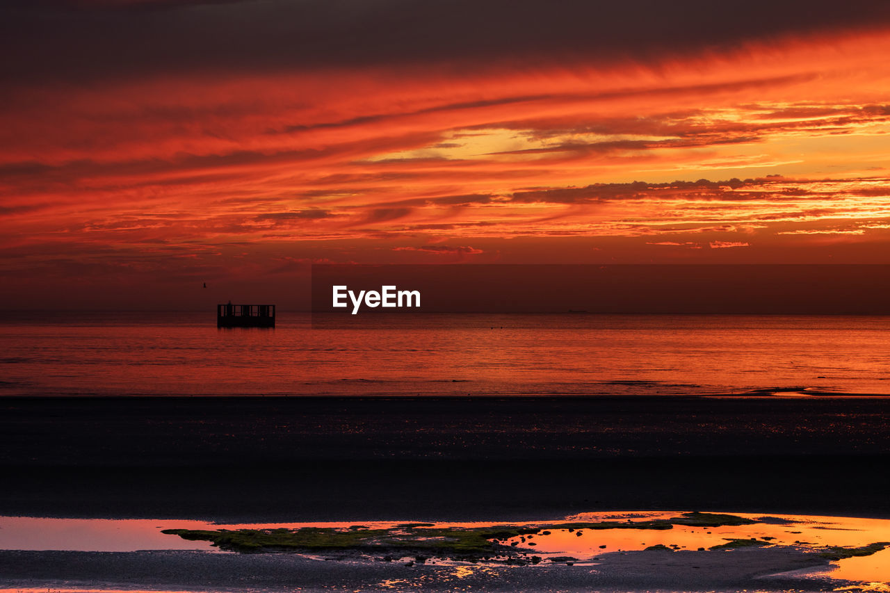 Scenic view of sea against dramatic sky during sunset