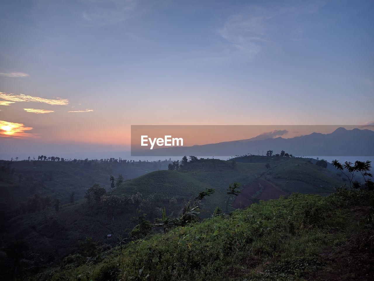 SCENIC VIEW OF FIELD BY MOUNTAINS AGAINST SKY DURING SUNSET