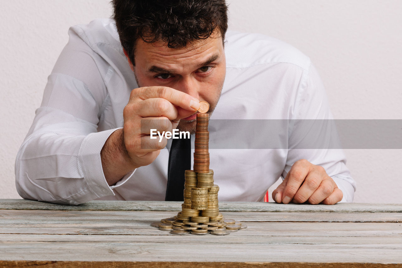 Man building stack of coins on table against white background