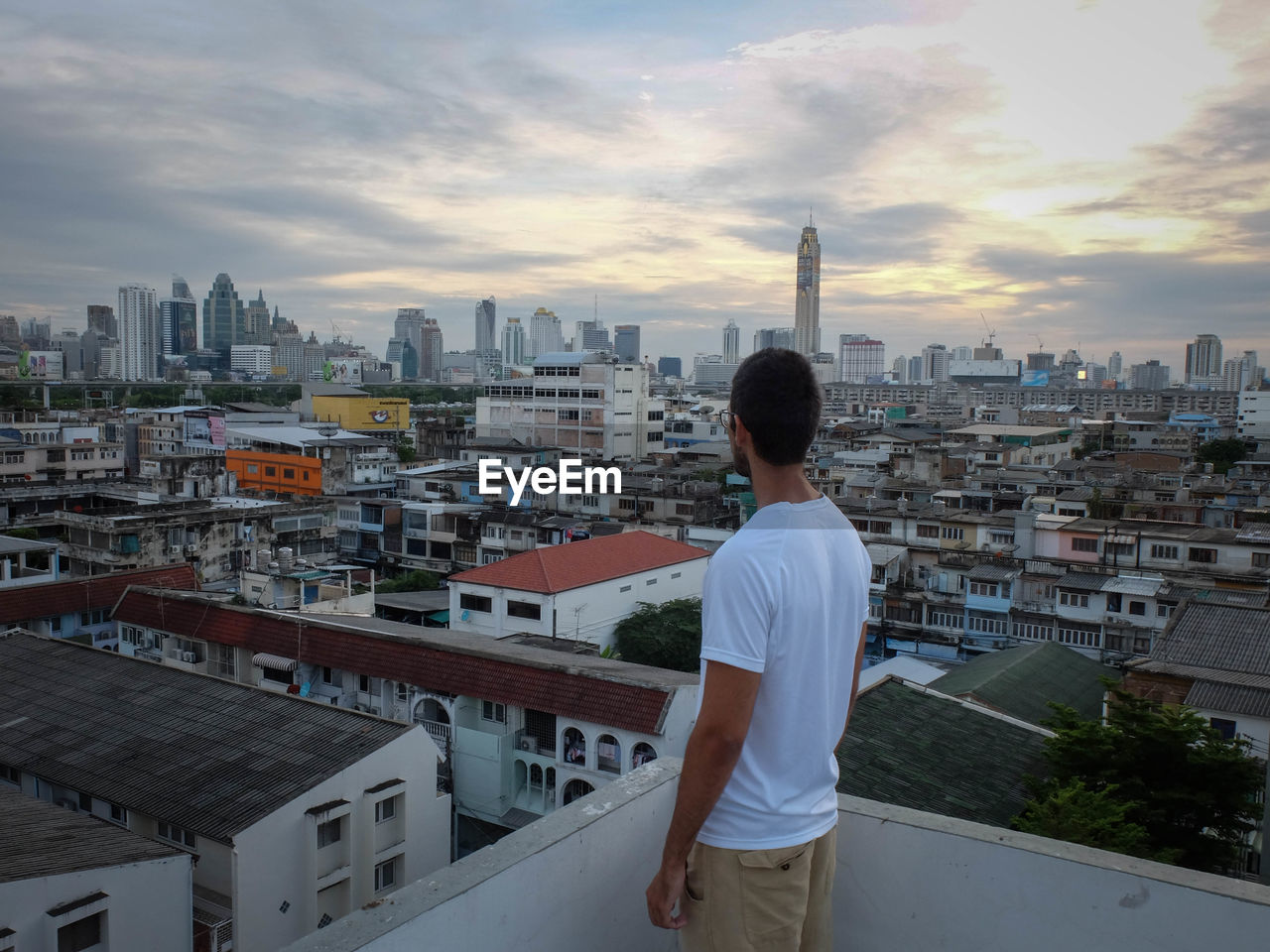 Man looking at cityscape while standing on building terrace against cloudy sky