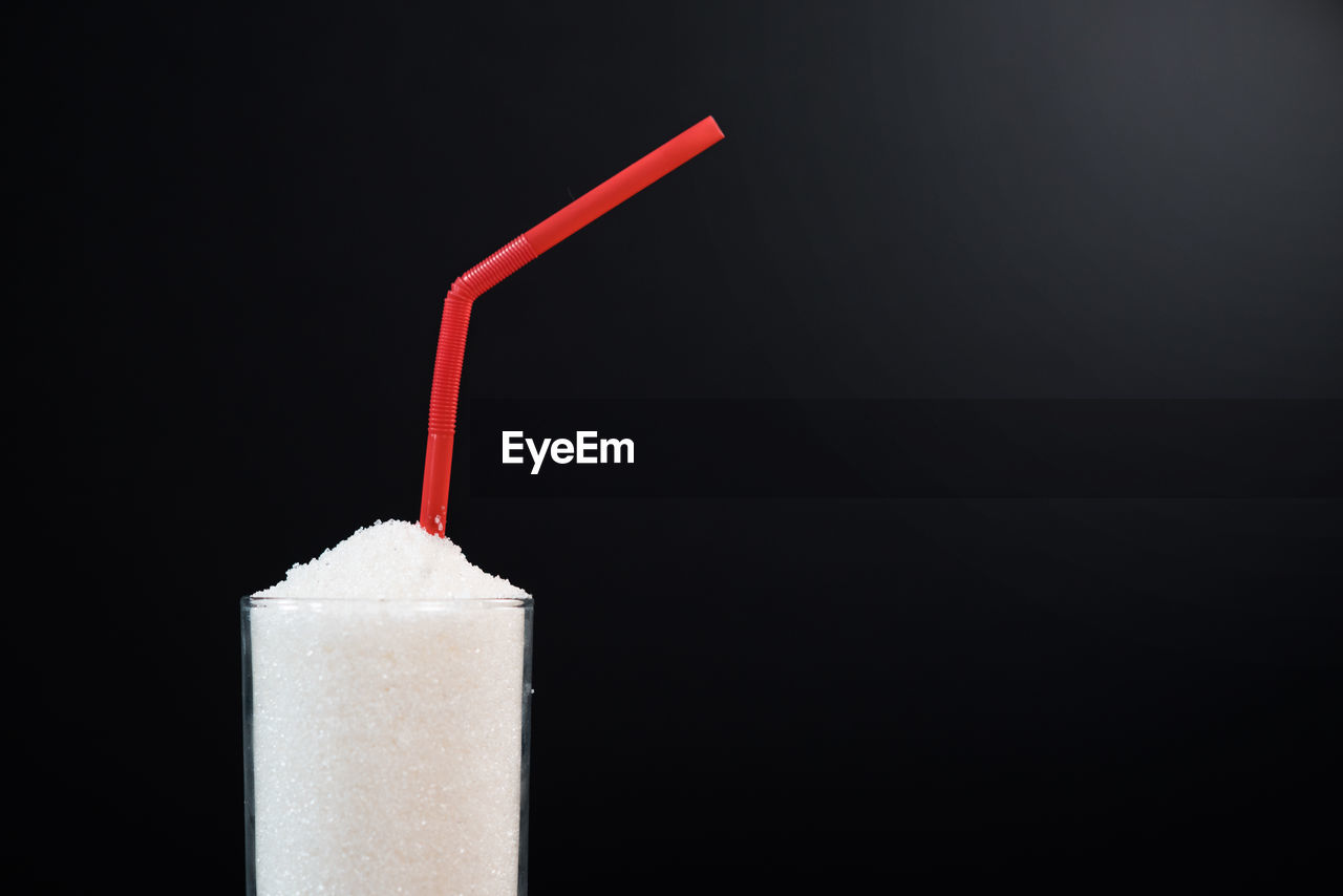 A glass white sugar with straw against black background. concept of unhealthy eating and diabetis