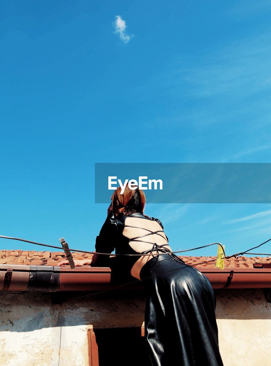 Low angle view of woman supported on roof against sky