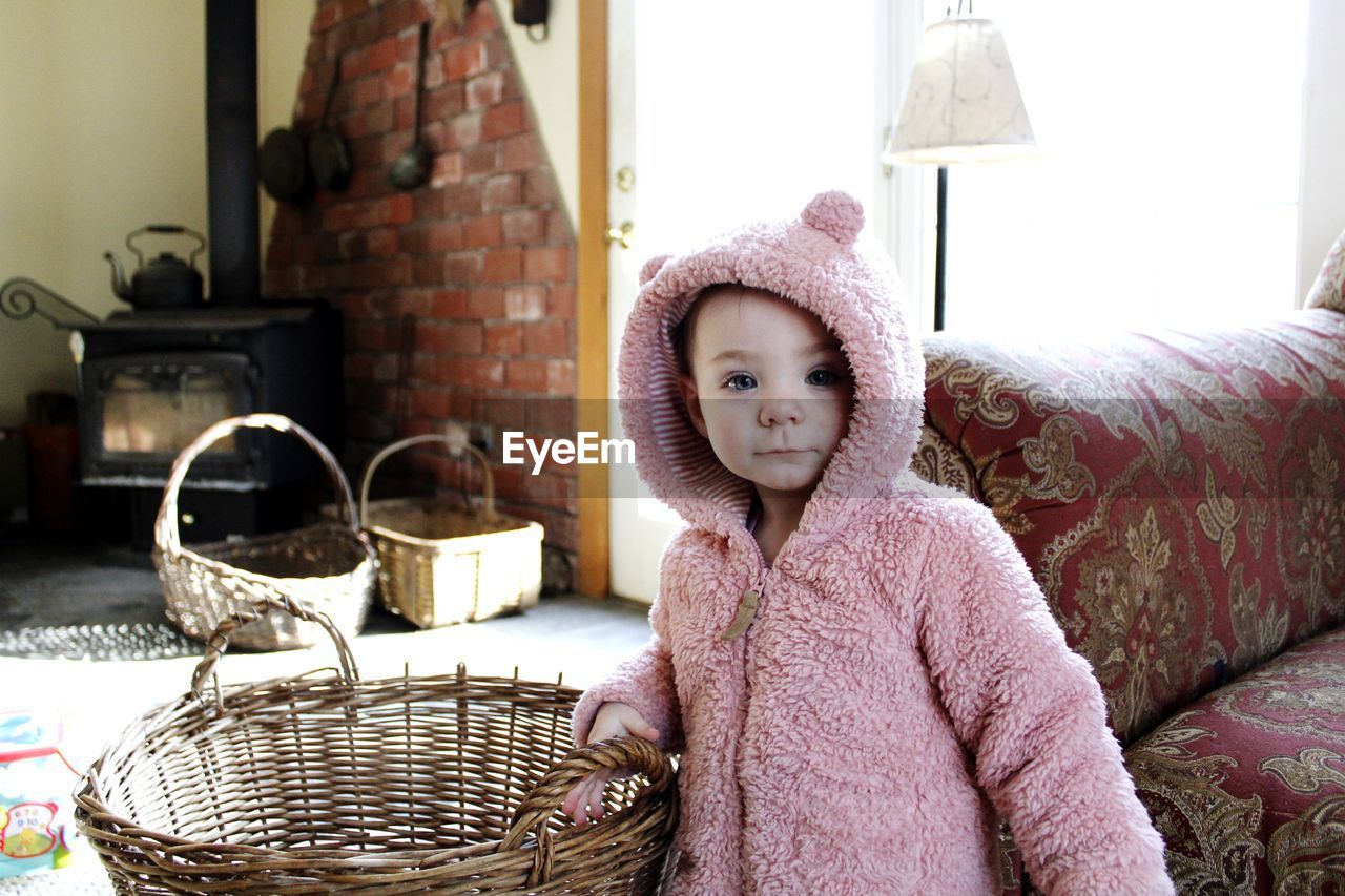 Portrait of cute baby girl by basket and sofa at home