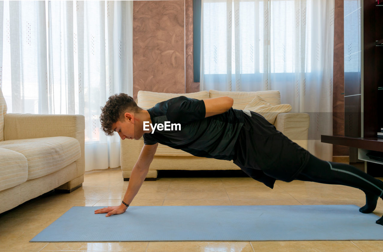 Side view of young man exercising on mat at home