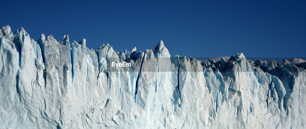 Panoramic view of frozen landscape against clear blue sky