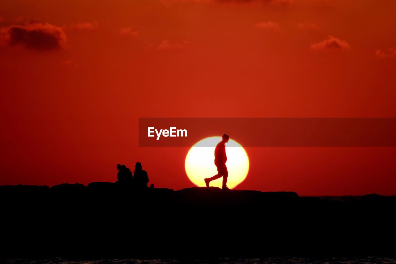 Silhouette men on pier against orange sky