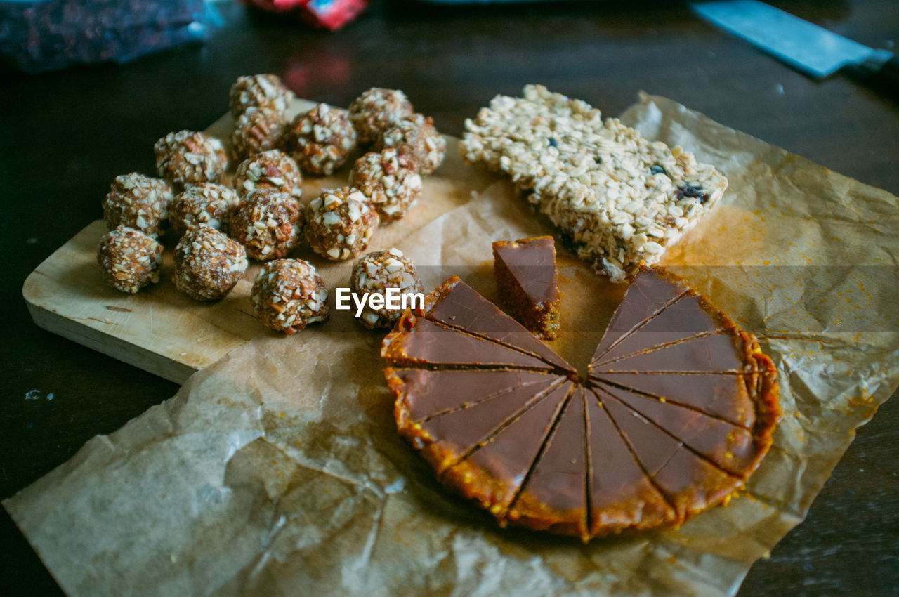 High angle view of chocolate tart and almond balls with nut bar on cutting board