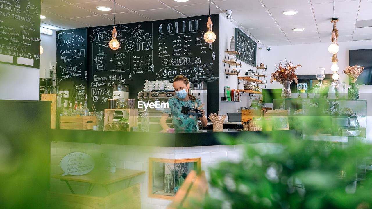 Woman wearing mask cleaning counter in cafe