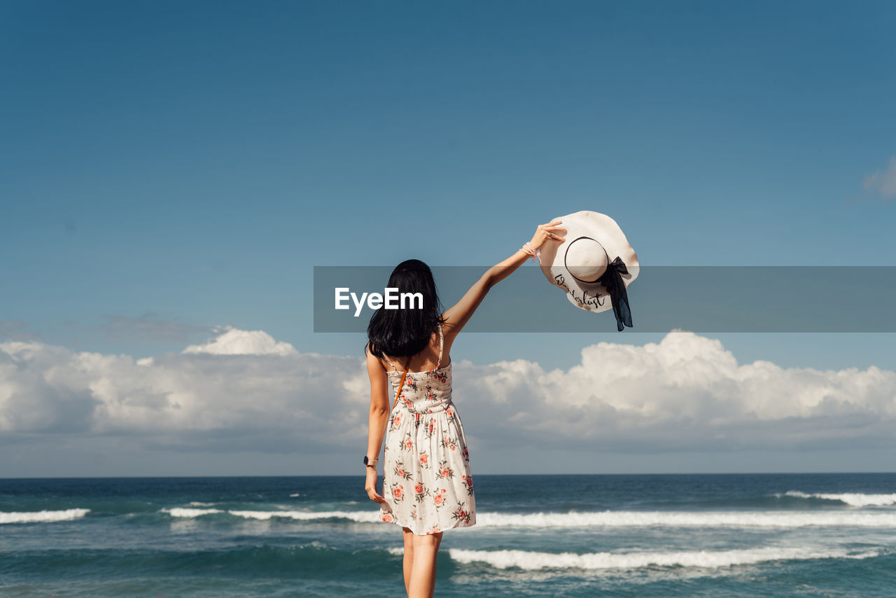 REAR VIEW OF WOMAN STANDING ON BEACH