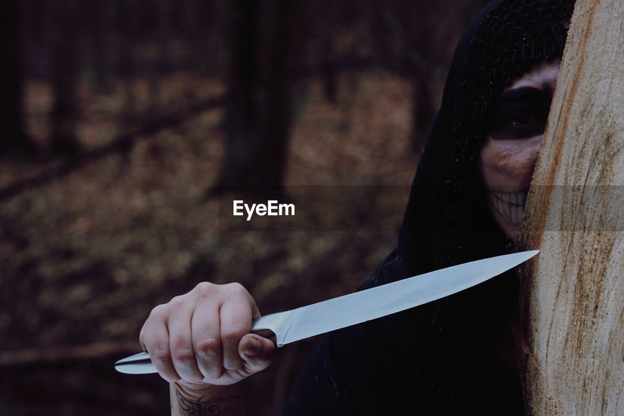 Girl wearing skull mask while holding knife during halloween