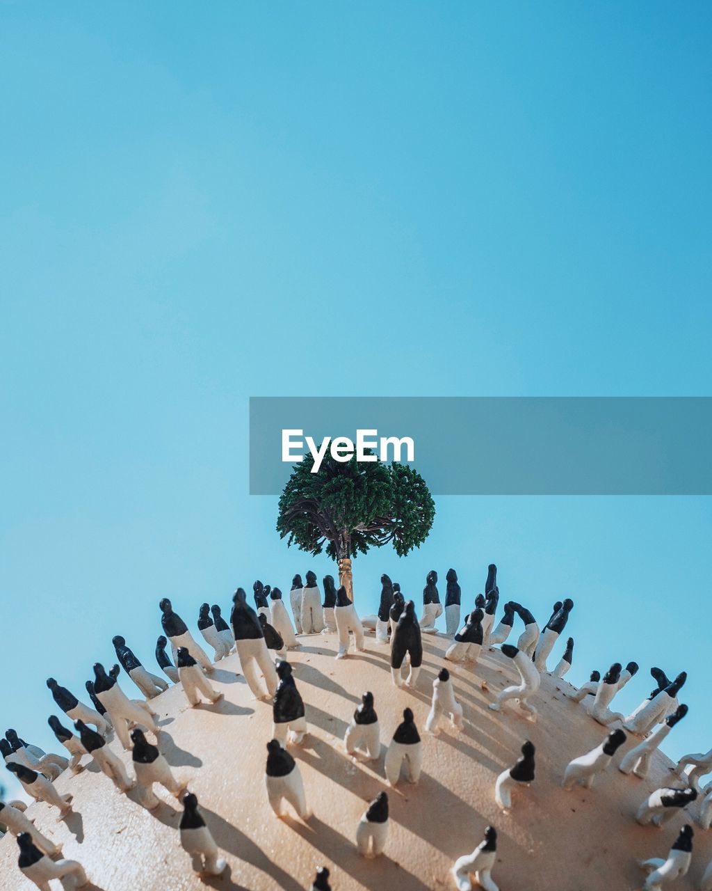 Artificial tree surrounded by figurines against clear blue sky