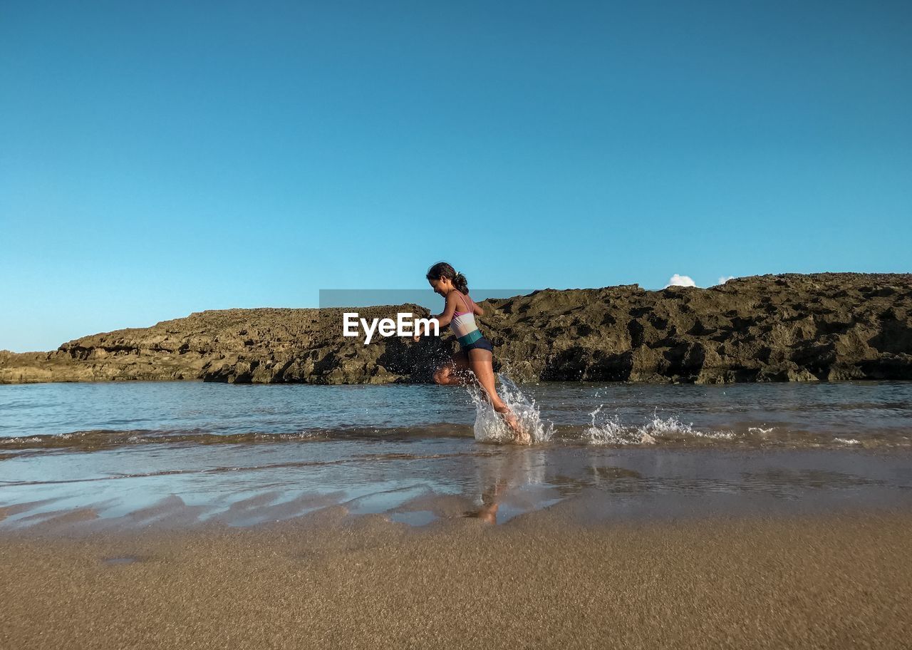 Girl running on beach against clear blue sky