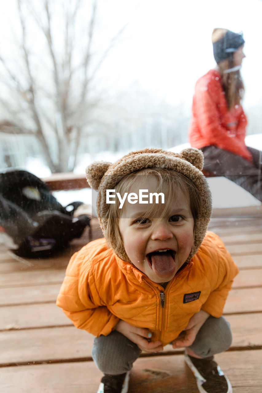 Three year old smiling girl looks through window with tongue out