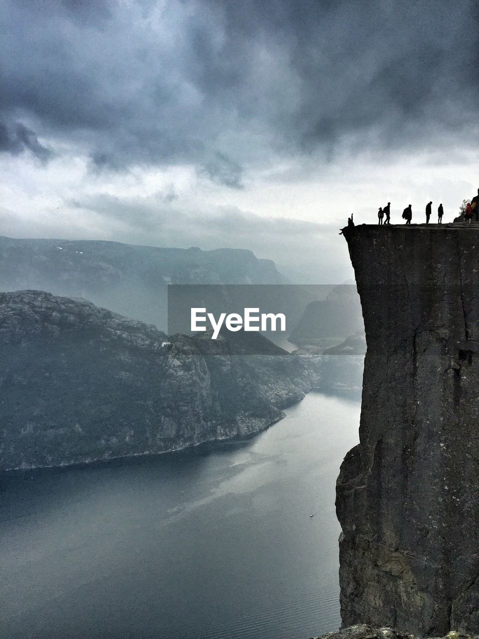 Silhouette people standing at preikestolen by river against cloudy sky