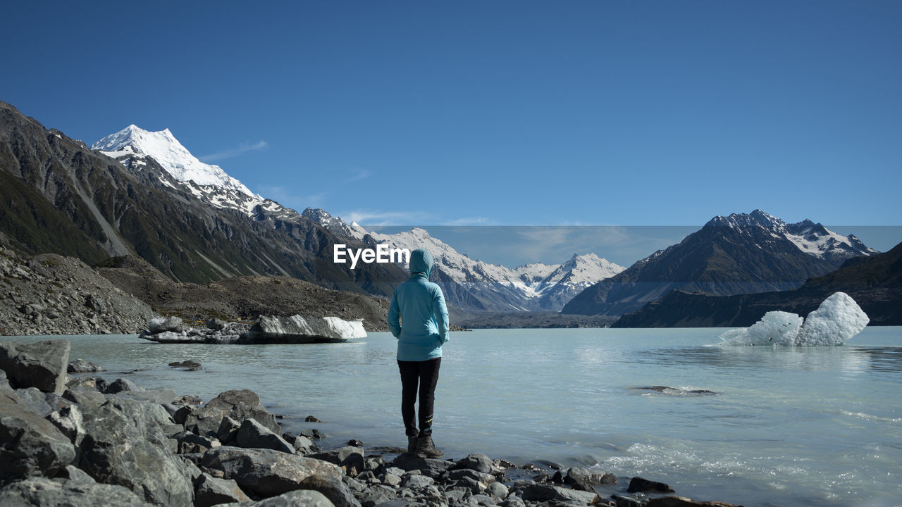 Tourist standing on the shore of tasman glacier terminal lake looking at snow-capped mountains