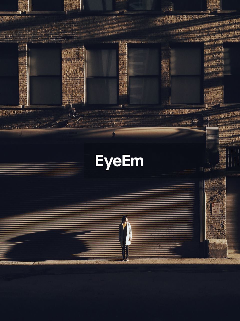 Mid distant view of woman standing on footpath against building