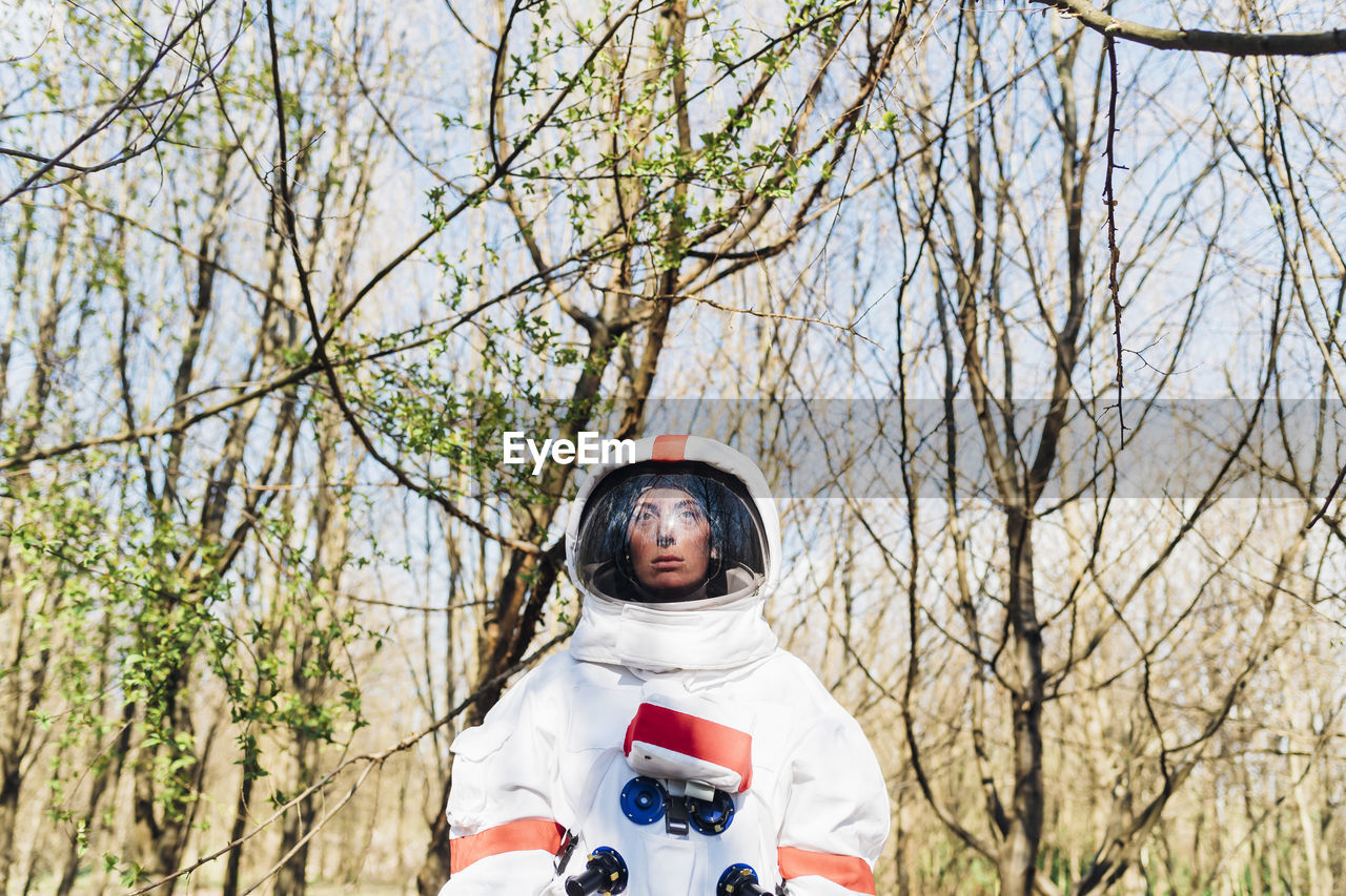 Female astronaut wearing space suit and helmet standing in forest