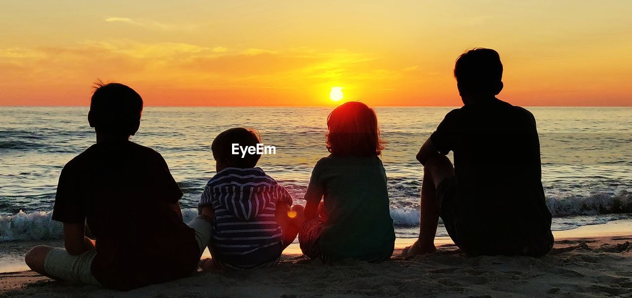 Rear view of people sitting at beach during sunset