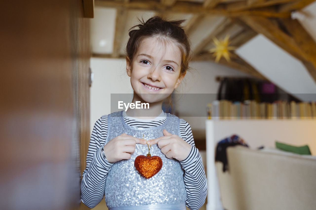 Smiling girl holding heart shape decoration at home