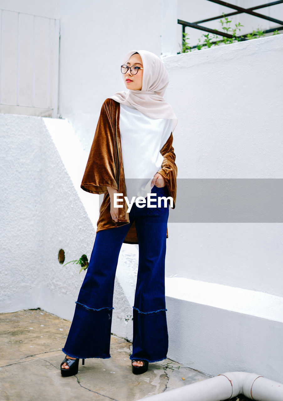 FULL LENGTH PORTRAIT OF WOMAN STANDING AGAINST WALL